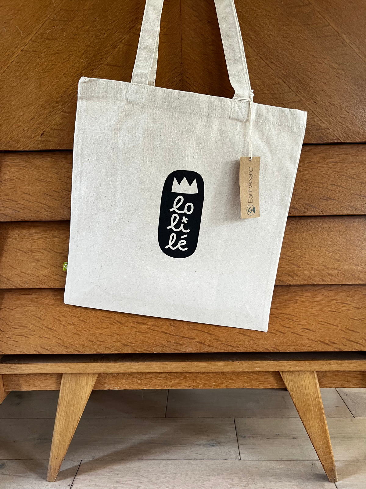 Tote bag « Jeu, set et lune » de Lolilé, représentant un petit personnage noir en tenue de tennis tenant une raquette et jouant avec une grande lune sur fond quadrillé bleu clair.