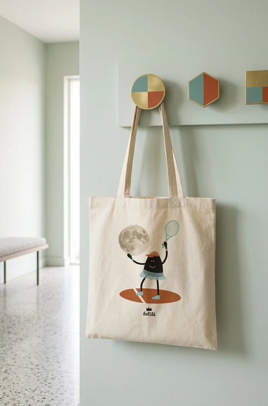 Tote bag « Jeu, set et lune » de Lolilé, représentant un petit personnage noir en tenue de tennis tenant une raquette et jouant avec une grande lune sur fond quadrillé bleu clair.